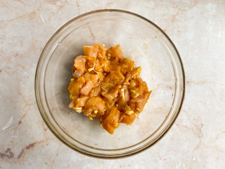 Na tigela, frango em cubos temperados com o alho, açafrão, sal e pimenta.