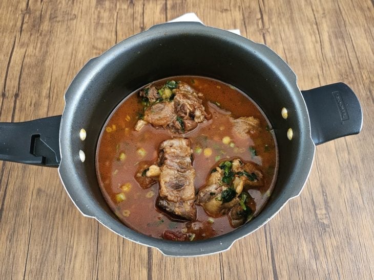 Uma panela com rabada, cebolinha e salsinha no caldo.