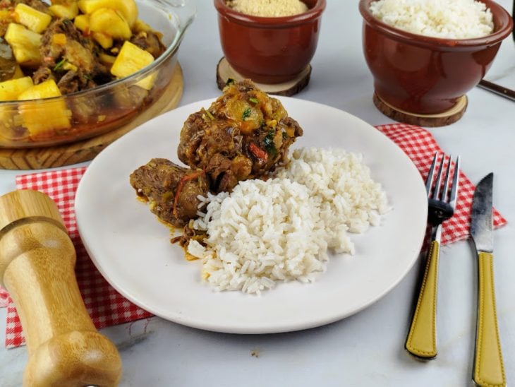 Rabada com mandioca servida com arroz branco em um prato raso e branco.