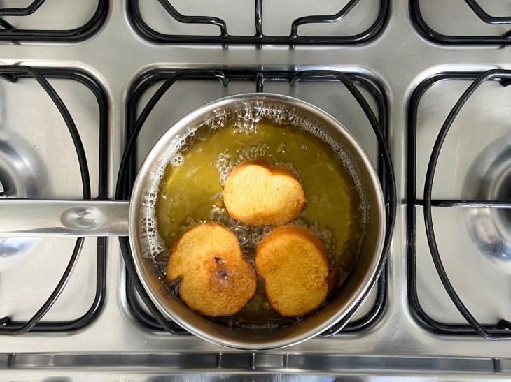 3 rabanadas sendo fritas em óleo na panela.