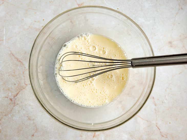 Mistura de leite condensado, ovos, leite, baunilha e amido sendo batida com fouet;