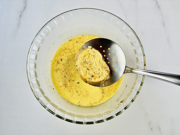 Fatias de pão sendo mergulhadas na mistura da tigela.