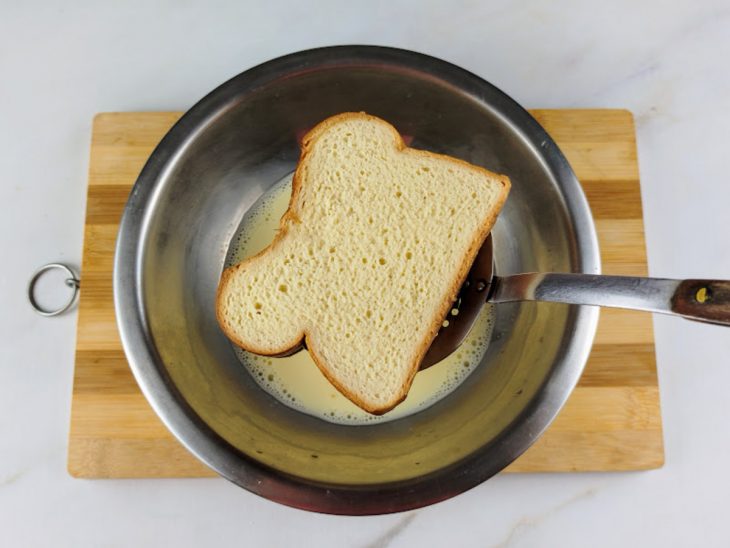 Fatia de pão sendo inserida na tigela com a mistura líquida.