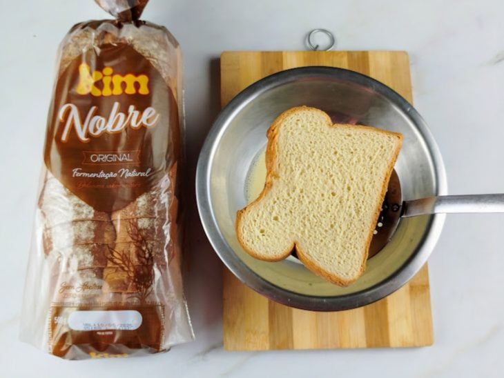 Fatia de pão sendo inserida na tigela com a mistura líquida.
