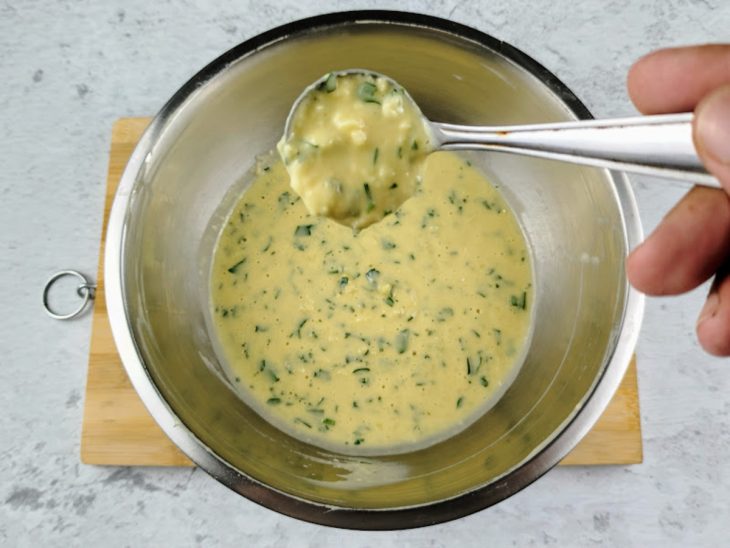 Uma tigela com ovos, sal, cheiro-verde, creme de leite, queijo ralado e farinha de trigo, e uma concha mostrando a consistência.