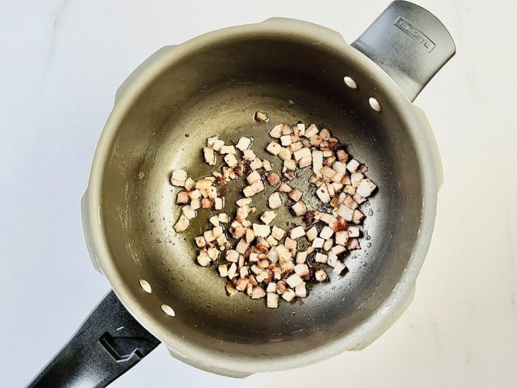Bacon em cubos fritando em uma panela de pressão com um fio de azeite.