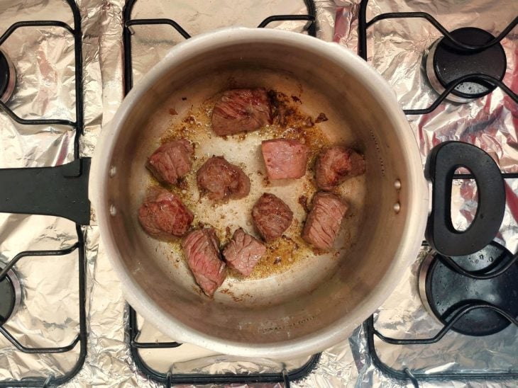 Alguns pedaços de carne sendo dourados em uma panela de pressão.