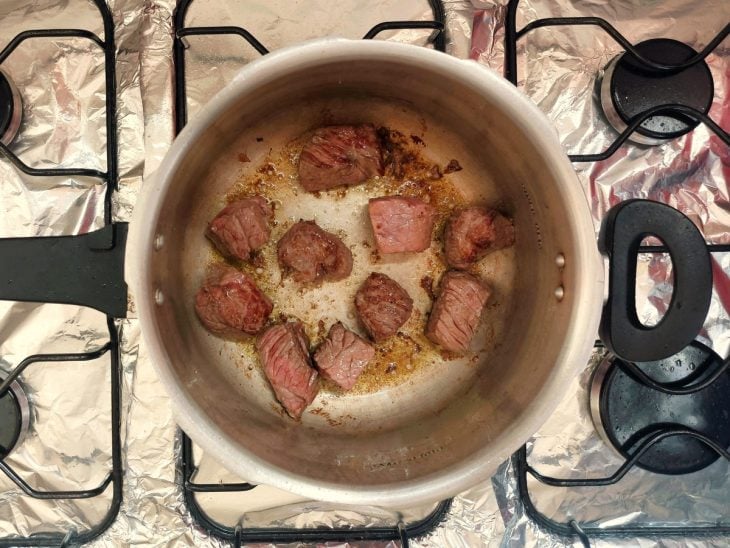 Alguns pedaços de carne sendo dourados em uma panela de pressão.