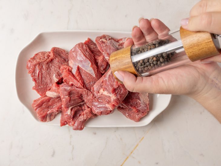 Carne sendo temperada com sal e pimenta-do-reino.