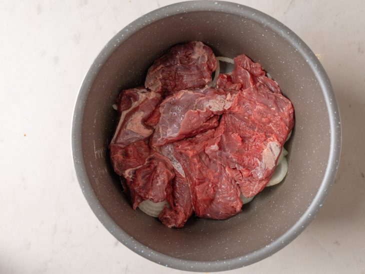 Carne temperada colocada na panela sobre uma camada de cebola.