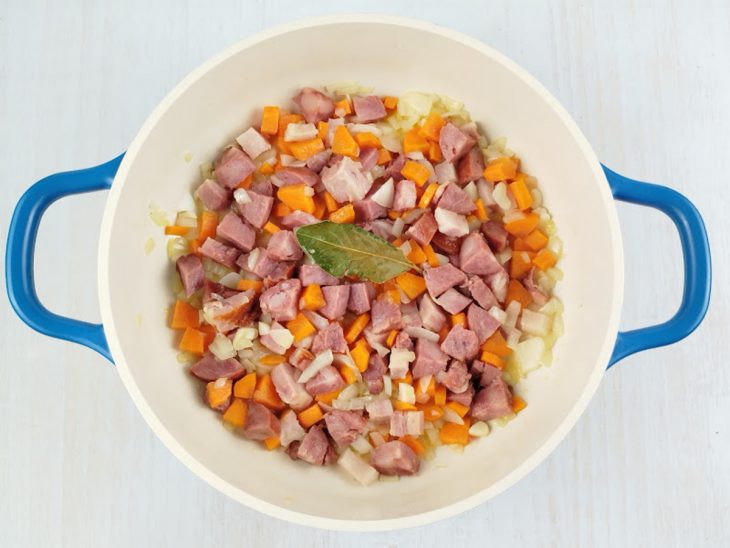 Em outra panela, a cebola, a folha de louro, o alho, o bacon, o paio e a cenoura.