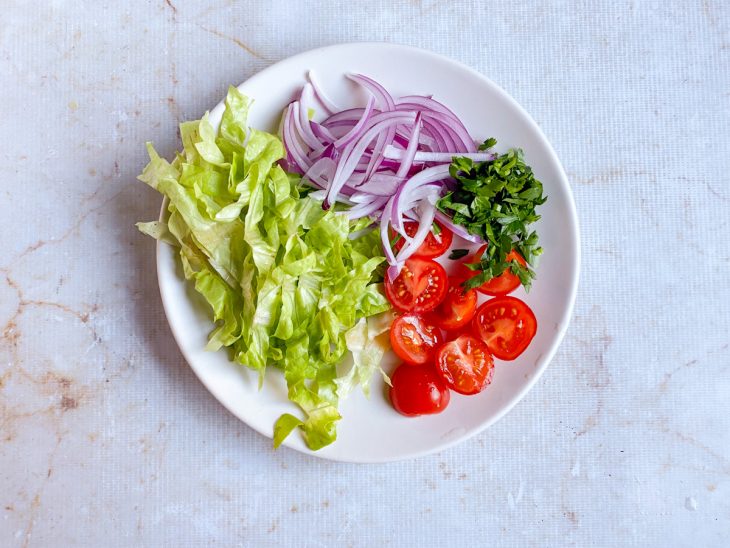 Alface, tomates, cebola e cheiro verde, cortados num prato.