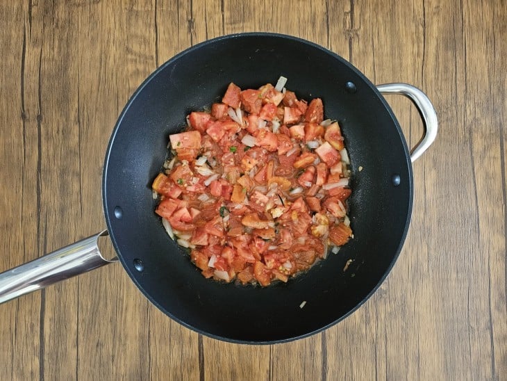 Uma frigideira com tomates picadinhos sendo refogados.