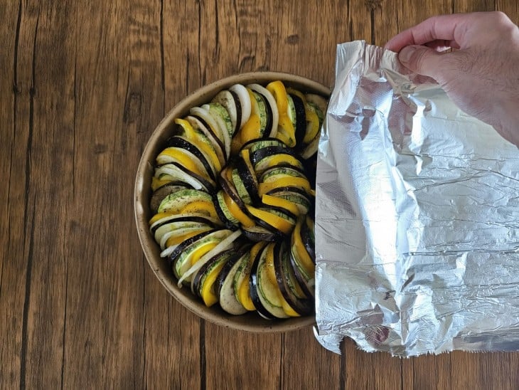 Uma forma com o ratatouille cru sendo coberto com papel alumínio.