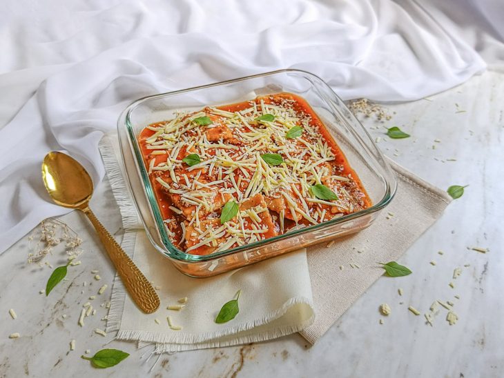 Raviolis finalizados com molho quente e queijo ralado.
