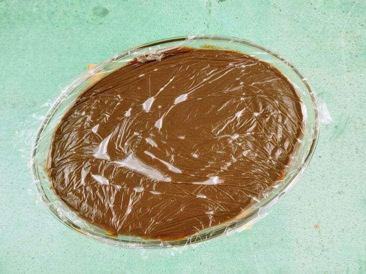 Uma travessa com o recheio de chocolate coberto com plástico-filme.
