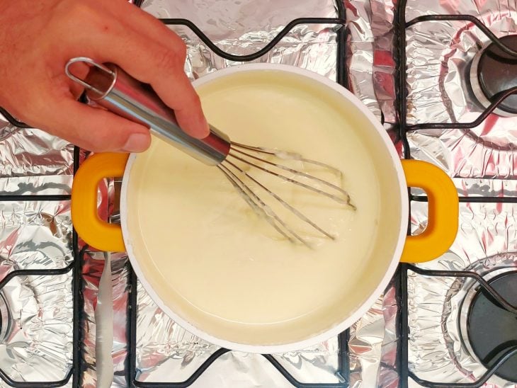 Uma panela com leite condensado, amido de milho, leite em pó, leite e manteiga cozinhando.