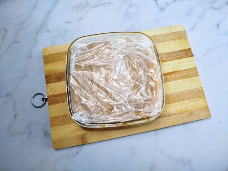 Um recipiente contendo recheio de doce de leite, coberto com plástico.