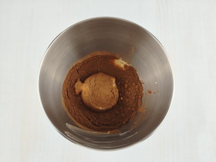 Doce de leite, creme de leite e chocolate em pó sendo adicionados à tigela.