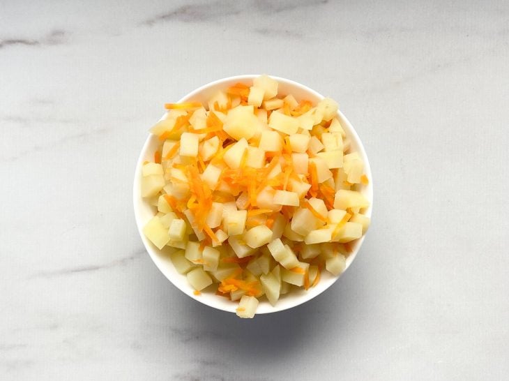 Um recipiente contendo batatas e cenouras cozidos.