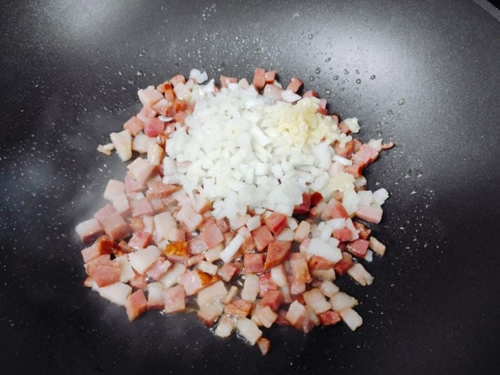 Alho e cebola adicionados a frigideira com bacon e calabresa.