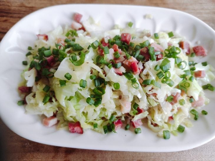 Repolho refogado com bacon e calabresa finalizado com cebolinha e salsinha em um refratário branco.