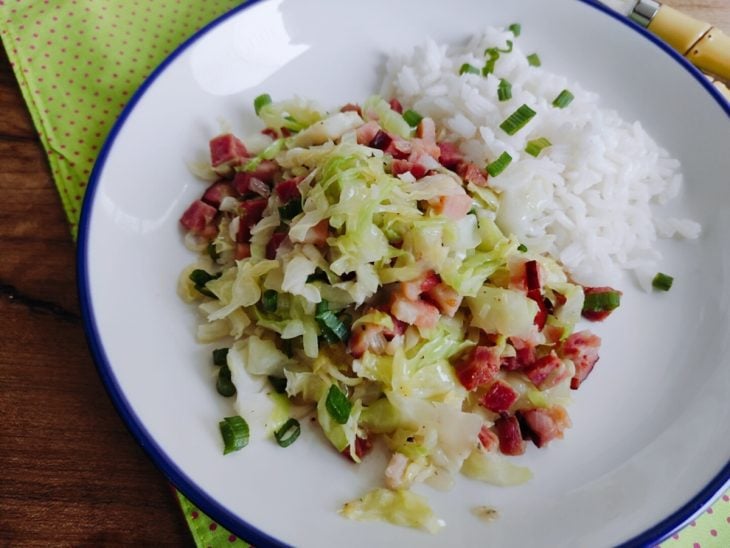 Repolho refogado com bacon e calabresa servido com arroz branco em um prato.