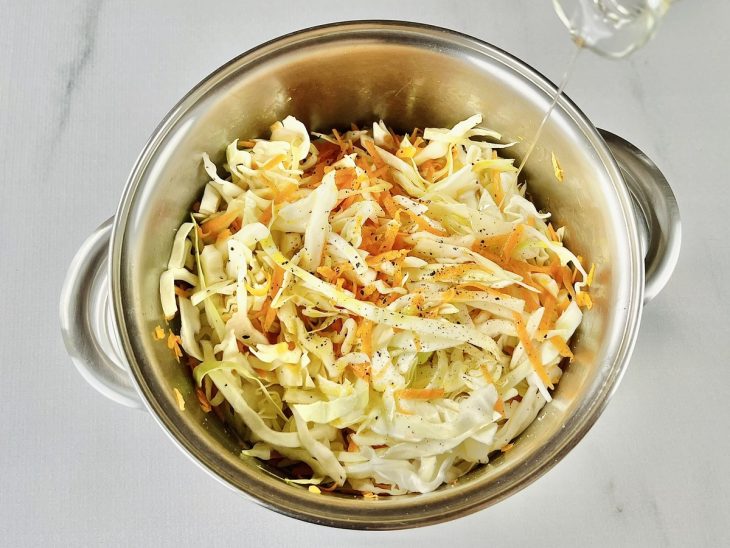 Repolho e cenoura temperados com sal, pimenta e azeite adicionados na panela.