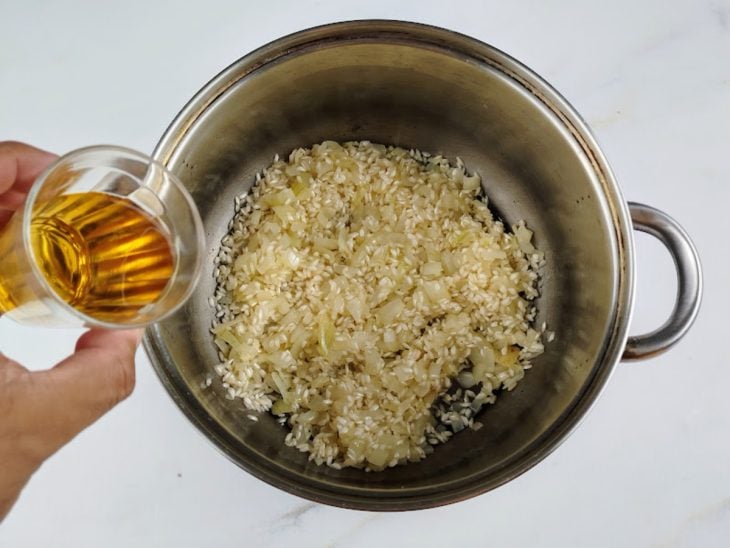 Vinho branco sendo adicionado à panela com o arroz e a cebola.