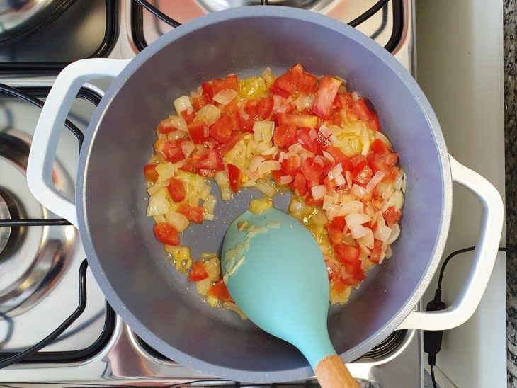 Uma panela com cebola, pimenta e o tomate sendo refogados.