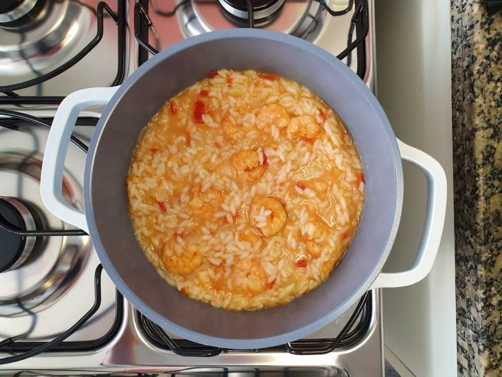 Uma panela contendo risoto sendo finalizado com camarão.