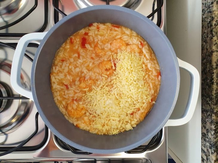 Uma panela contendo risoto sendo finalizado com queijo.