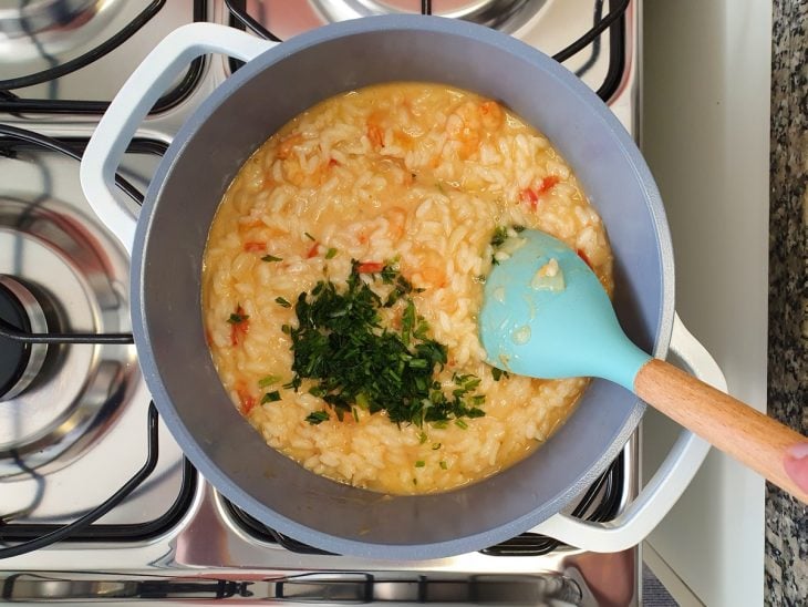 Uma panela contendo risoto sendo finalizado com salsinha.