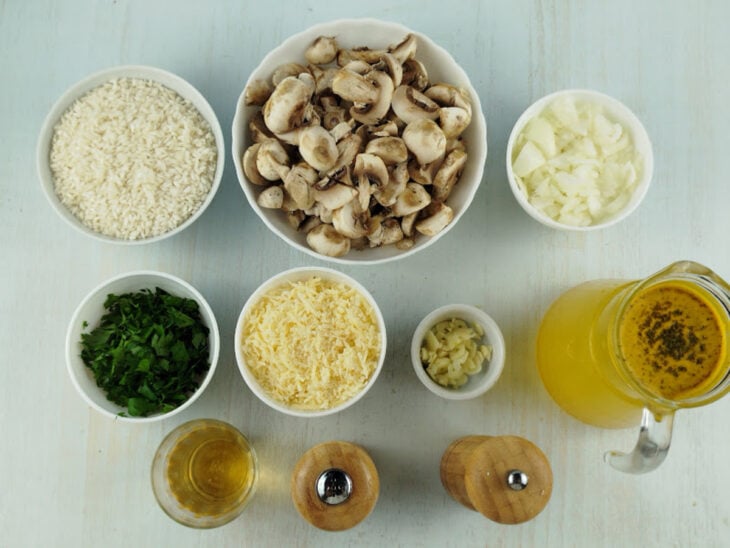 Ingredientes organizados na bancada com arroz arbóreo, champignon, cebola, alho, parmesão e demais temperos separados.