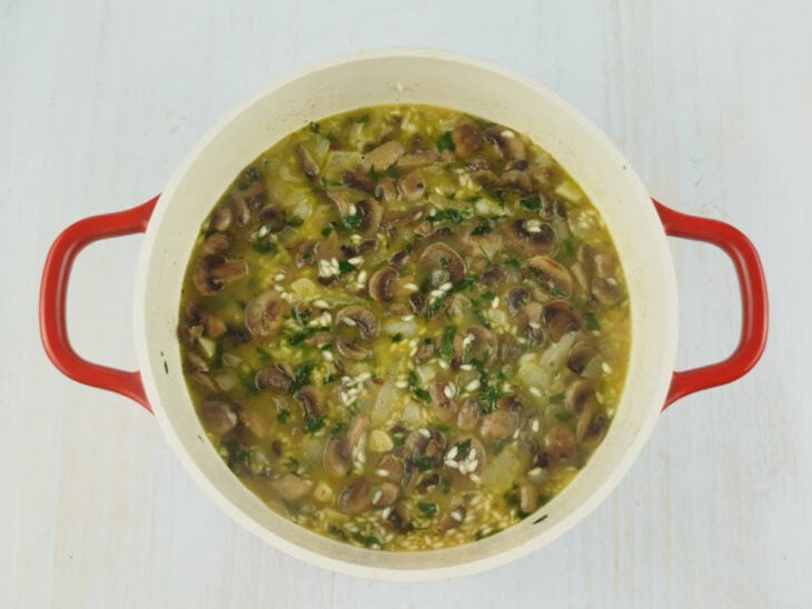 Caldo de legumes quente e vinho branco sendo adicionados aos poucos enquanto o risoto é mexido delicadamente.