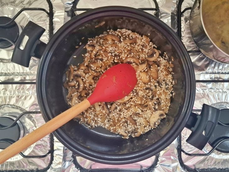 Cebola sendo refogada em uma panela com manteiga. Arroz arbóreo Caldo Bom sendo adicionado.