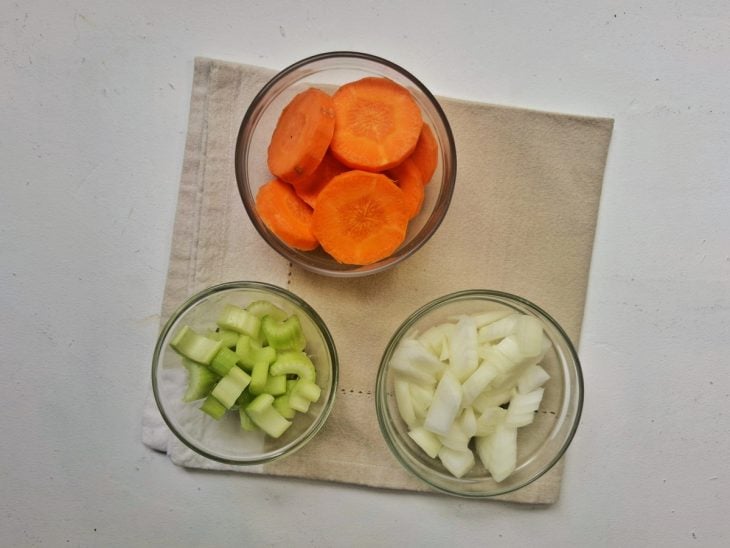 Cenoura, salsão e cebola picados e dispostos em vasilhas.