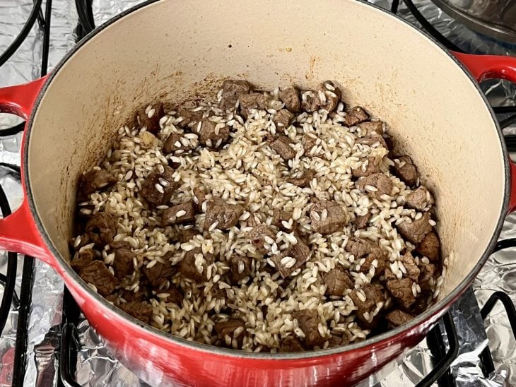 Uma panela com cubos de filé mignon, cebola, arroz e alho refogados na manteiga.