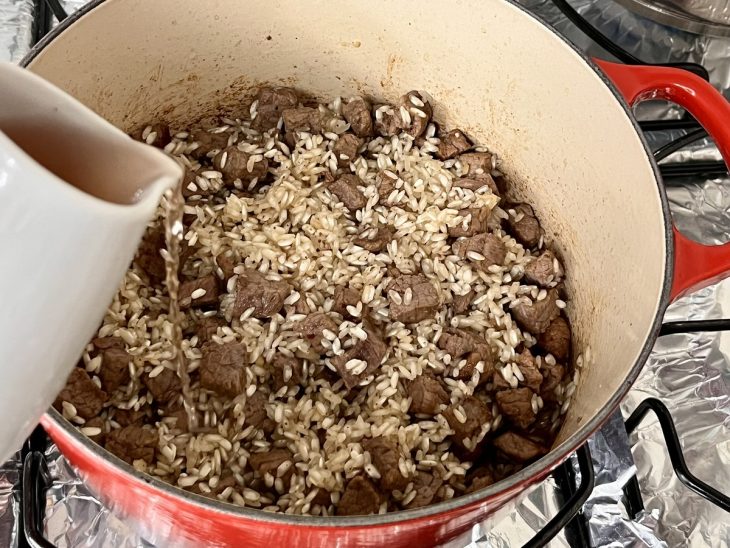 Uma panela contendo cubos de filé mignon, cebola, arroz e alho refogados na manteiga com vinho branco.