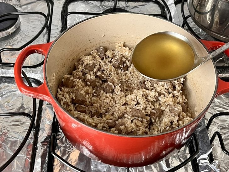 Uma panela contendo cubos de filé mignon, cebola, arroz e alho refogados na manteiga com caldo de legumes.