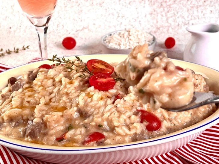 Um recipiente contendo risoto de filé mignon com pupunha e tomate-cereja.