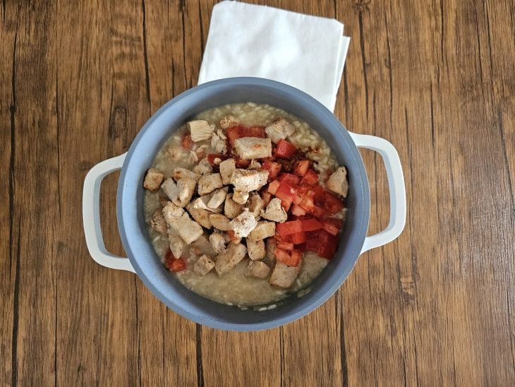 Uma panela cozinhando arroz arbóreo com caldo de legumes, cubos de frango e temperos.