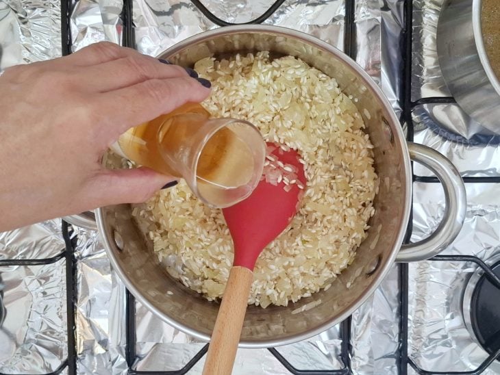 Vinho branco adicionado na panela com arroz arbóreo e cebola.