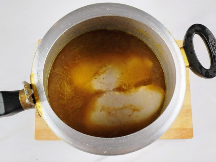Peito de frango com água e temperos em uma panela de pressão.