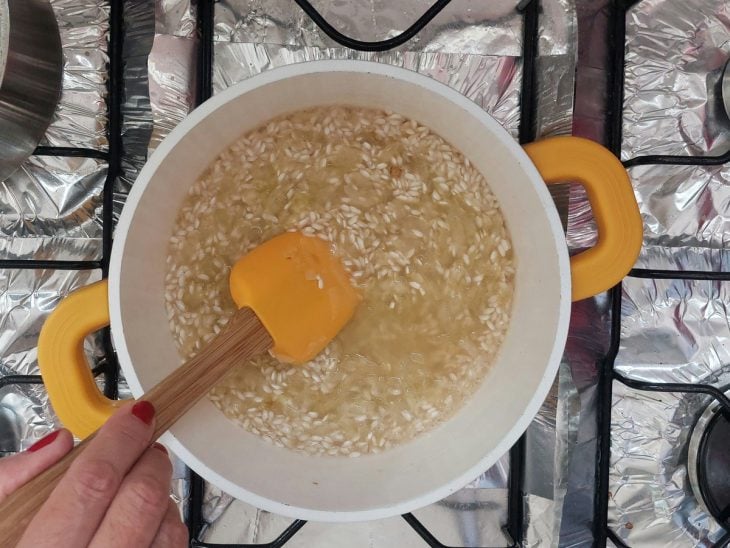 Uma panela com cebola, azeite, arroz, vinho e temperos.