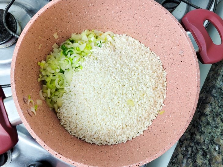 Uma panela refogando salsão, cebola, alho-poró e arroz no azeite.