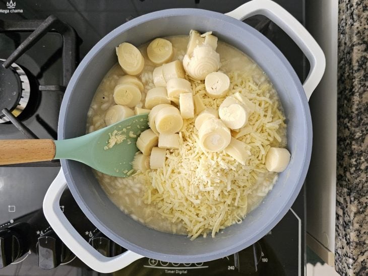 Uma panela contendo risoto sendo finalizado com queijo e palmito.