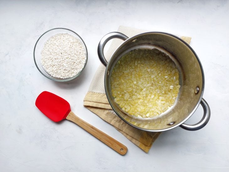 Arroz ao lado da panela com azeite e cebola picada.