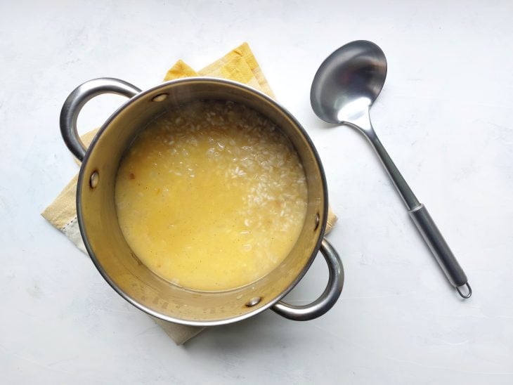 Arroz com caldo em uma panela e concha ao lado.