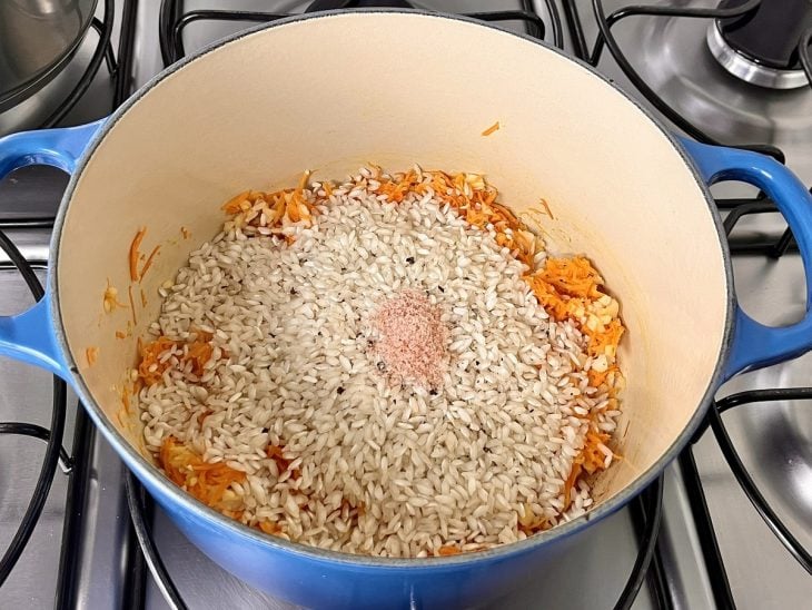 Uma panela refogando cebola, cenoura ralada e o arroz.